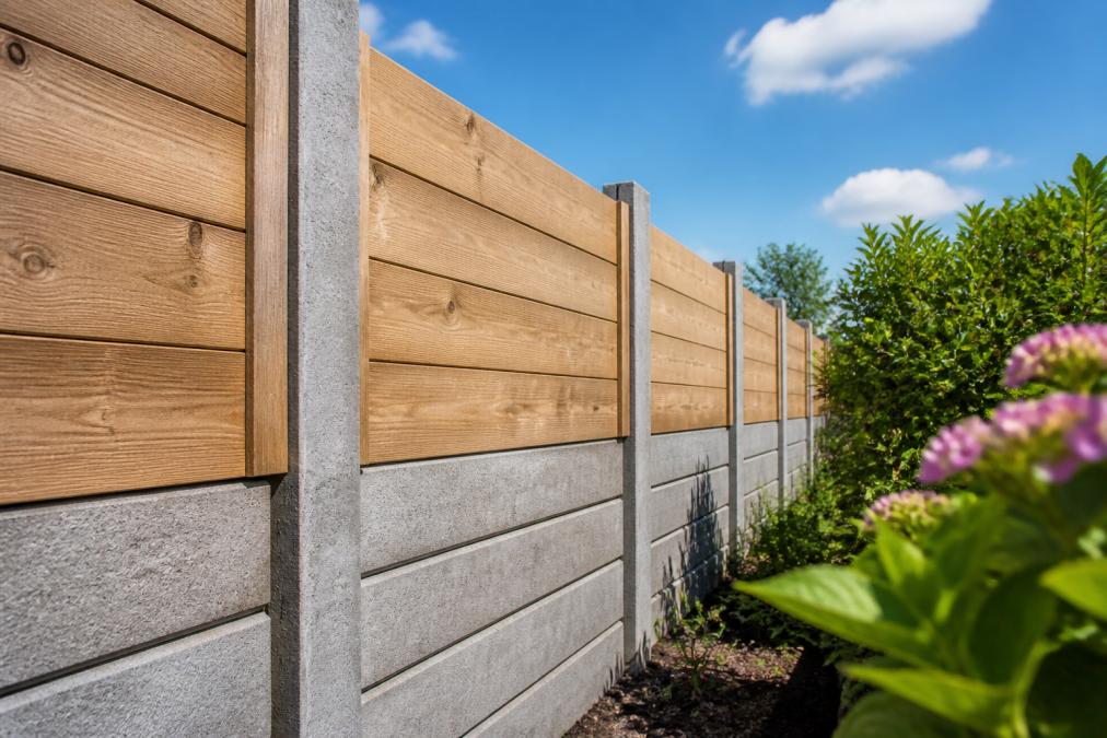 Close-up van een hout-betoncombinatieschutting in een tuin met houten planken boven en betonnen palen, in natuurlijk daglicht onder blauwe hemel