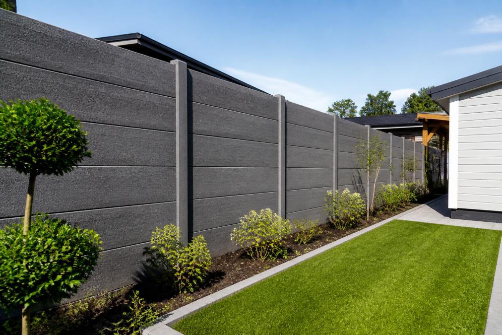 Goed onderhouden betonnen schutting rond een recreatiewoningtuin, met scherpe lijnen en minimale verwering na jaren van gebruik, in natuurlijk daglicht